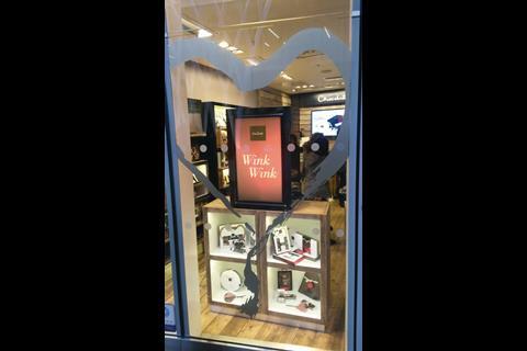 The exterior-facing side carries the message “Wink Wink” in a white font set against a rose-pink background, while on the other side there is a picture of, yes, a heart-shaped box of chocolates.